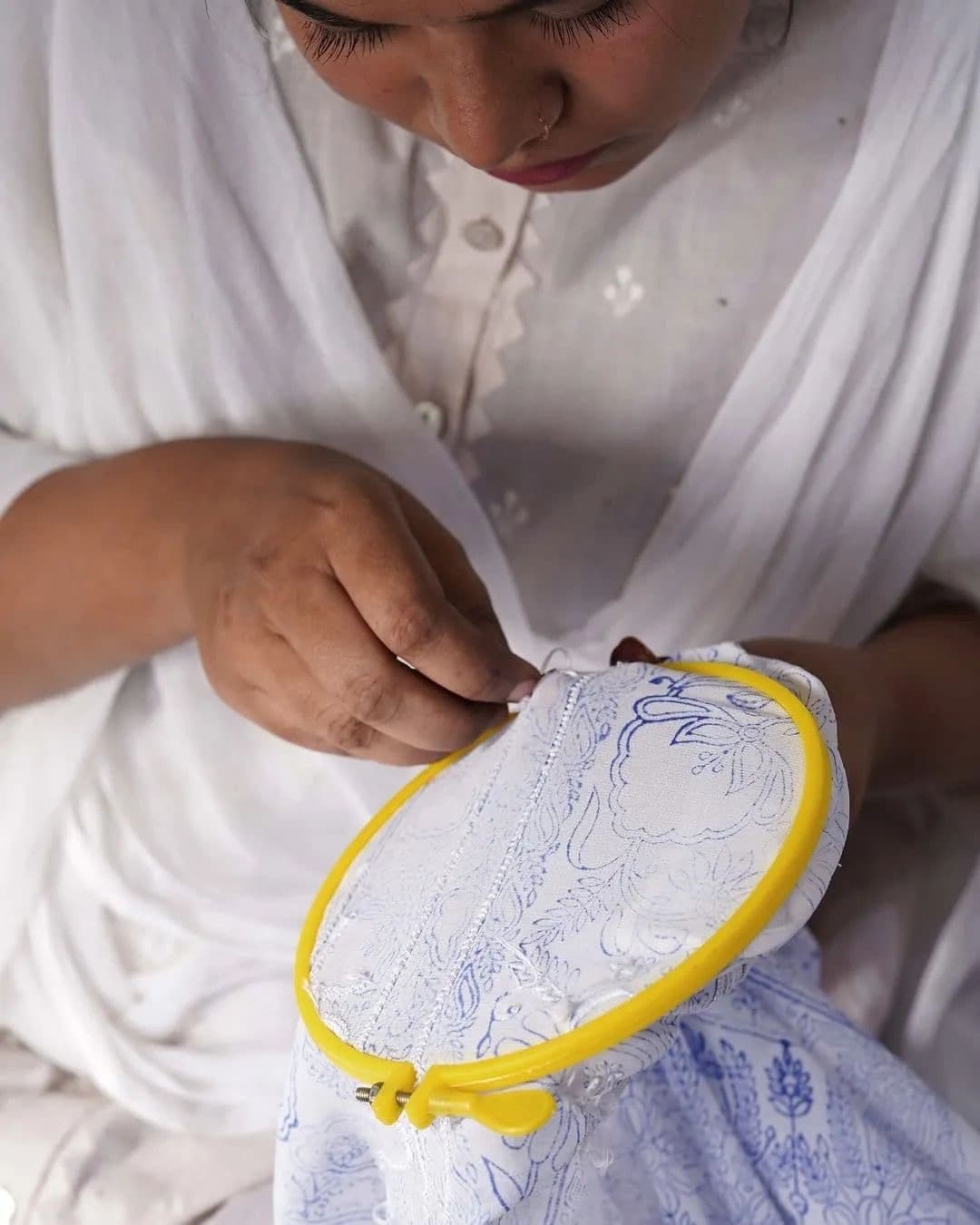 An artisan stitching a garment seam inside a hoop